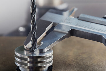 vernier caliper measures metal drill bit, make holes in steel billet on industrial drilling machine. Metal work industry.