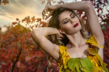 Beautiful girl in dress from yellow foliage in autumn forest with red leaves. Portrait of sexy young female model