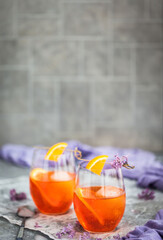 Orange Aperol Spritz cocktail served in a wine glasses, decorated with slice of orange and lilac
