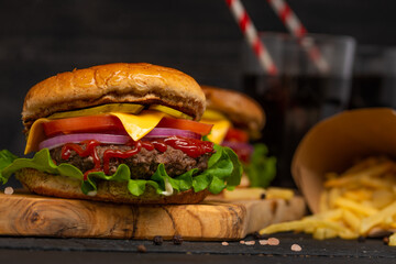Tasty burger with soda. Juicy meat, green salad, cheese, slice of tomato, ketchup and tasty sous. Sweet coca-cola for drink. Dark background. Fast food. Enjoy your meal. Big burger for hungry.