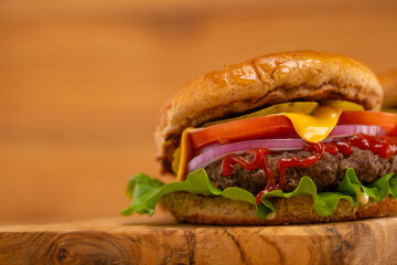 Tasty burger on the wood cutting board. Light background. Slice of cheese, tomato, onion. green salad and steak. Ruddy bread. Wooden design. For restaurant menu. Fast food.
