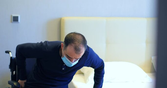 Disabled man in wheelchair with protective mask transferring to bed. Dolly shot 4k