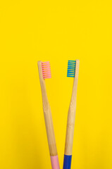 dos cepillos de dientes uno rosa y otro azul de bambú con fondo liso de color amarillo  