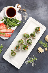 Japanese cuisine. Rice rolls with red fish, arugula and crab meat with soy sauce on a white plate on a gray background. Background image, copy space