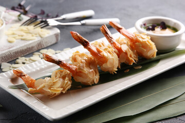 Seafood. Fried shrimp prawns in almond chips with sauce on a white plate in a restaurant. Bamboo leaves on a gray table. Background image, copy space
