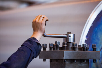 Worker's hand on lathe tool holder of metal turning machine. Low depth of field.