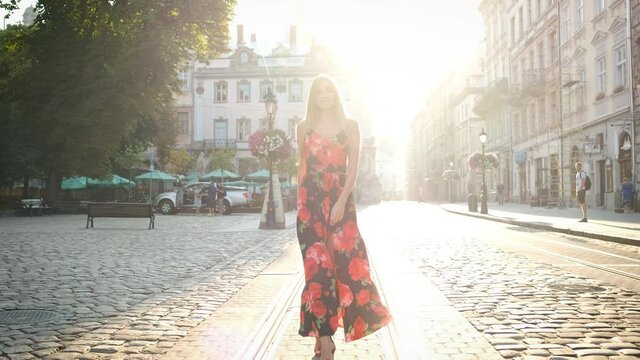 Beautiful blonde Caucasian appearance with a sincere smile and a beautiful long dress with a strut walks around the morning city. Posing in front of the camera Tourist. Model