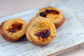Naklejka na ściany i meble Traditional Portuguese popular dessert Pastel de nata or Pastel de Belem on a white wooden board. Delicious puff pastry cups with custard. Gastronomic travel in Portugal.