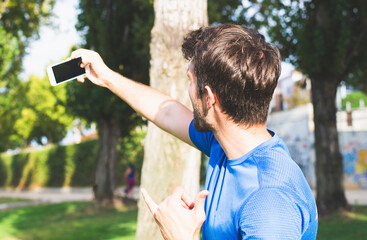 Attractive young man makes a selfie with his smartphone dressed in sportswear in the park.