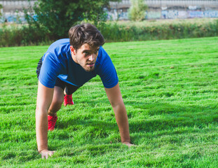 Bearded man dressed in sportswear in the park looks forward while doing push-ups.