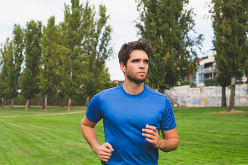Young man with a beard and blue shirt runs through the park in summer.
