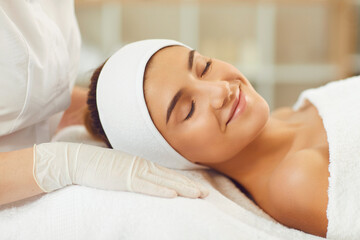 Fototapeta na wymiar Young woman smiling with eyes closed lying on spa bed after skin care procedures