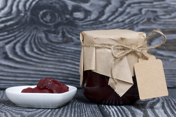 A jar of cherry jam with a label for an inscription and a saucer of cherry marmalade. On pine planks painted black and white.