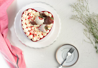 pastel redvelvet en forma de corazón sobre una mesa blanca con un trapo rojo al lado y un plato pequeño con un tenedor
