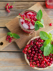 Glass of red currant cocktail or mocktail, refreshing summer drink with crushed ice and sparkling water on a wooden background.