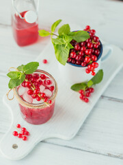 Glass of red currant cocktail or mocktail, refreshing summer drink with crushed ice and sparkling water on a white wooden background.