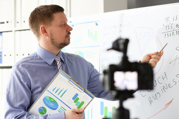 Male in suit and tie show stats graph pad making promo videoblog or photo in office camcorder to...