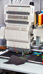Industrial embroidery machine with multicolored threads, close-up, vertical image.