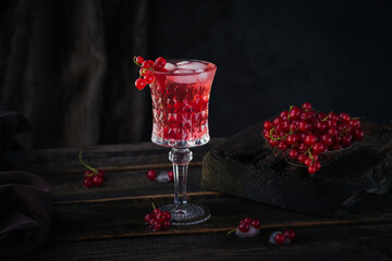 Glass of red currant cocktail or mocktail, refreshing summer drink with crushed ice and sparkling water on a dark wooden background