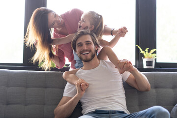 Happy cheerful parents having fun with cute children daughters cuddling playing on sofa together,...