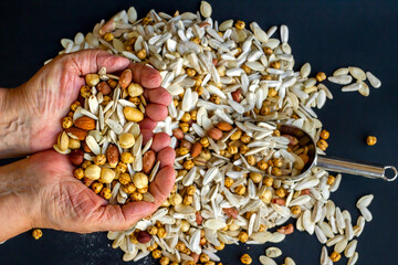 Mixed nuts in hand of old person on black background,top view