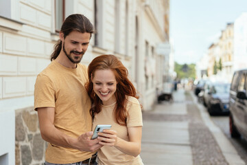 Young couple grinning while looking at a mobile