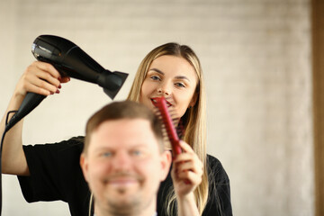 Young Hairdresser Drying Male Hair by Blow Dryer. Woman Hairstylist Using Hairdryer and Hairbrush for Styling Haircut. Man Client Getting Hairstyle in Barbershop Looking at Camera Photography