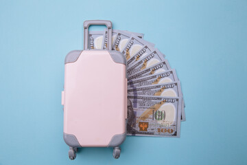 Mini travel luggage suitcase and money banknotes on blue background. Savings for traveling concept.