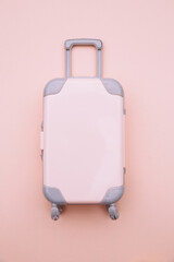 Mini travel luggage suitcase on pink background. Travel, summer vacation or tourism concept.