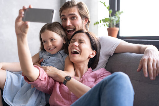 Cheerful family with children laughing taking selfie together on phone, young mom holding smartphone making photo of daughter at home, loving parents having fun with adopted kids and gadget