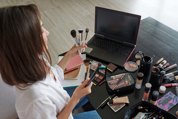 Girl make-up artist shows a set of makeup brushes, focus on laptop screen