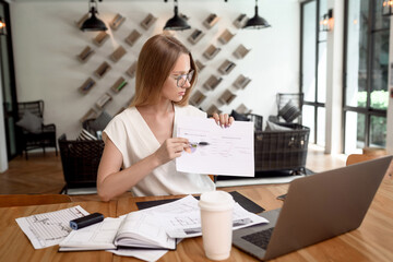 A girl in a business suit shows a diagram. Young woman working at a table with a laptop in the office. Female business, remote work.