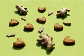 Homemade heart shaped gingerbread cookies and ginger root on a green background. Flat lay.