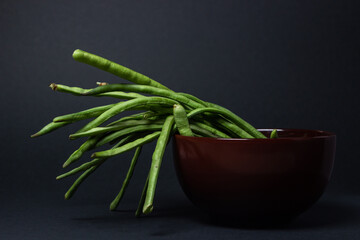 green beans on a black background. The green beans are on a brown plate. Harvesting