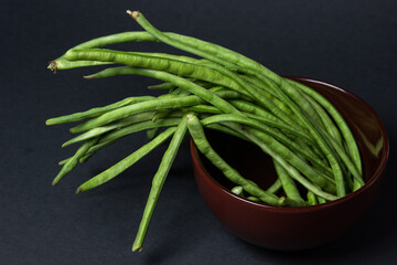 green beans on a black background. The green beans are on a brown plate. Harvesting