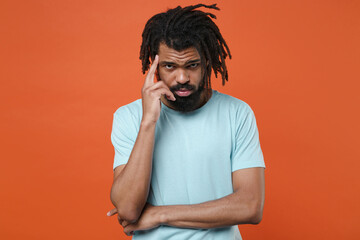 Pensive concerned young african american man guy wearing blue casual t-shirt posing isolated on bright orange background studio portrait. People sincere emotions lifestyle concept. Put hand on head.