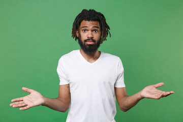Confused puzzled young african american man guy with dreadlocks 20s wearing white casual t-shirt...