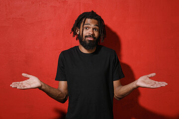 Confused puzzled young african american man guy with dreadlocks 20s wearing casual black t-shirt...