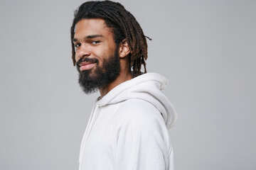 Side view of smiling handsome young african american man guy with dreadlocks 20s wearing white casual streetwear hoodie posing looking camera isolated on grey color wall background studio portrait.