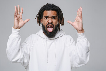 Angry irritated young african american man with dreadlocks 20s in white casual streetwear hoodie spreading hands screaming swearing looking camera isolated on grey color background studio portrait.