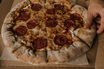 A large round juicy mouth-watering pizza with cheese and salami lies on a cardboard box from a delivery package. paper backing. close view. see flour. good thin dough
