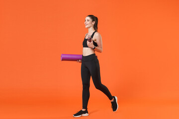 Fototapeta na wymiar Full length portrait of smiling young fitness sporty woman in black sportswear posing going training working out hold bottle of water yoga mat looking aside isolated on orange color background studio.