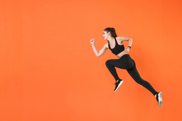 Fototapeta na wymiar Full length side view of portrait of young fitness sporty woman 20s wearing black sportswear posing training working out jumping like running looking aside isolated on orange color background studio.