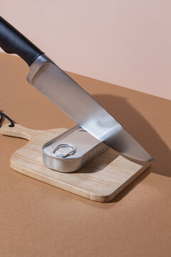 Sharp knife cutting metal tin with preserved food on cutting board