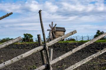 Fototapeta na wymiar vintage wooden mill behind a fence on a green hill against a blue sky background