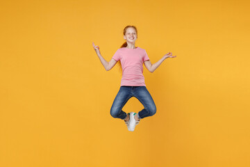 Fototapeta na wymiar Full length children studio portrait smiling little ginger kid girl 12-13 years old in pink casual t-shirt jumping hold hands in yoga gesture, relaxing meditating isolated on yellow color background.