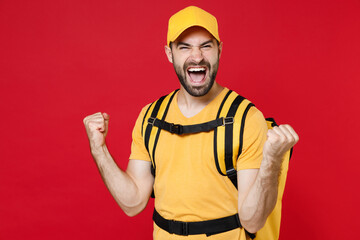 Delivery employee man guy male 20s in yellow cap t-shirt uniform thermal bag backpack with food work as courier isolated on red background studio. Service during quarantine coronavirus covid-19 virus.