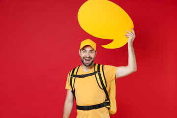 Delivery employee man guy male in yellow cap t-shirt uniform thermal food bag backpack work courier service during quarantine coronavirus covid-19 hold speech bubble isolated on red background studio.