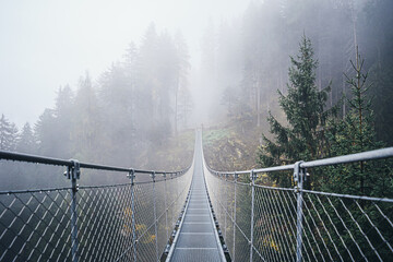 Fototapety  Suspended metal bridge over beautiful rabby valley in fog somewhere in northern Italy in early autumn.