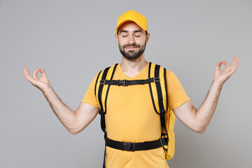Delivery employee man guy male 20s in yellow cap t-shirt uniform thermal food bag backpack work courier service during quarantine coronavirus covid-19 virus, posing isolated on gray background studio.